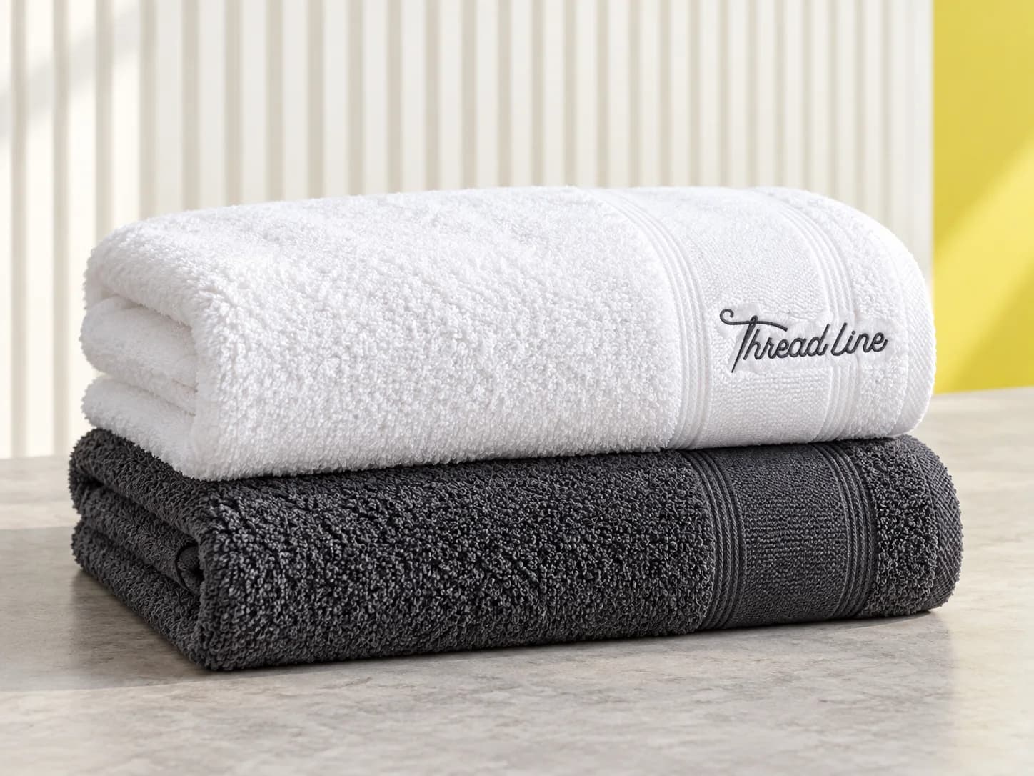 White and charcoal folded bath towels with a Threadline embroidered border