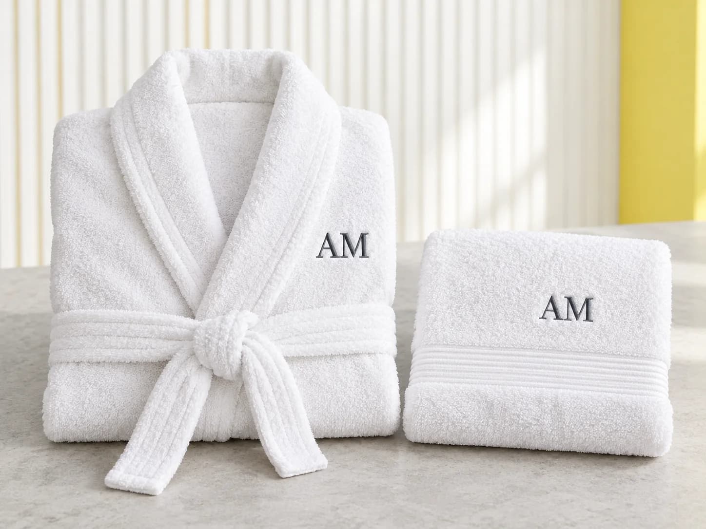 Folded white robe and matching towel with charcoal AM monograms