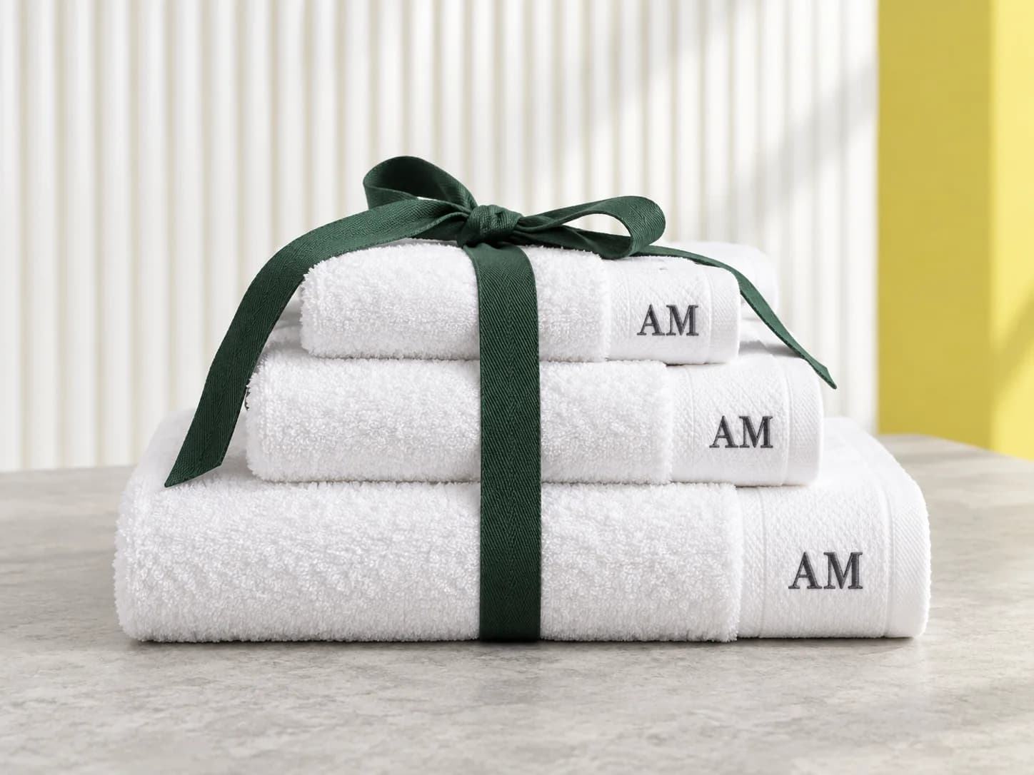 Three white towels embroidered AM and tied with a green ribbon