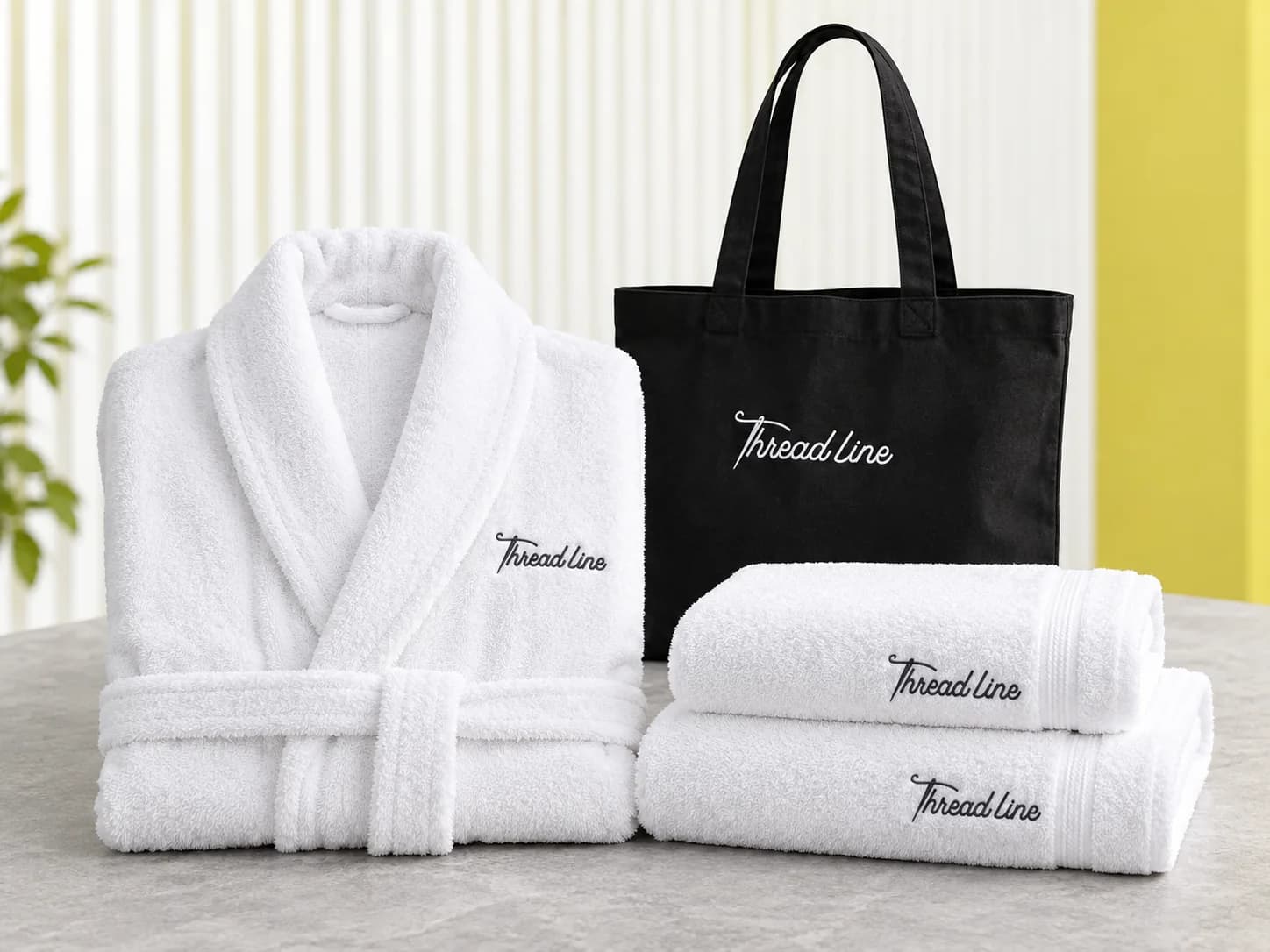 White embroidered robe and towels beside a black Threadline canvas tote